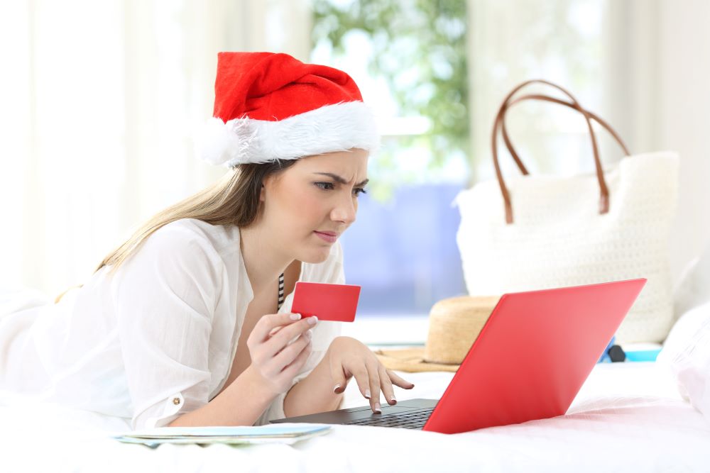 Woman on the computer holding a credit card while wearing a Santa hat