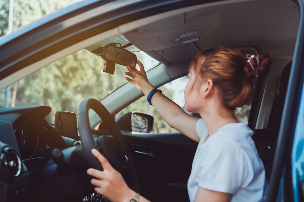 A woman is sitting inside a car and is adjusting her mirror.