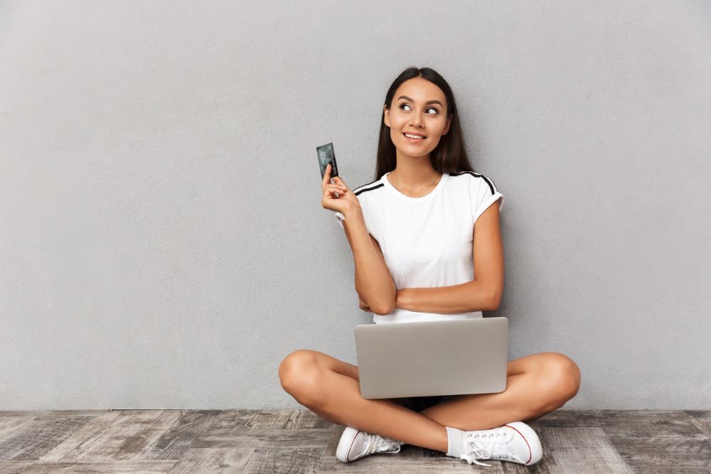 Woman sitting isolated over grey background using laptop computer holding credit card.