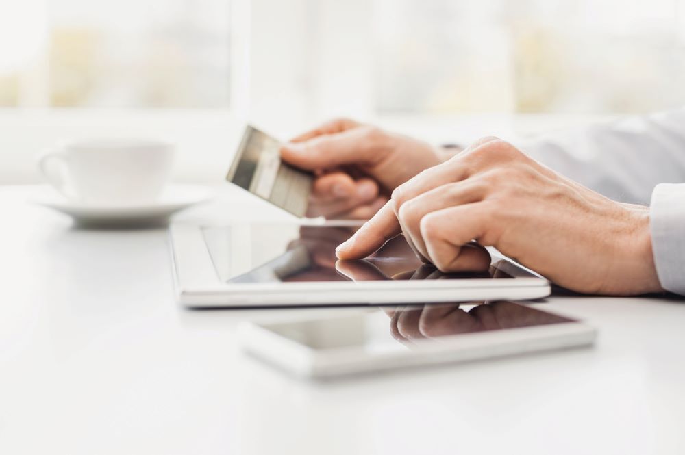 A Man is shopping online with his tablet while holding his credit card.