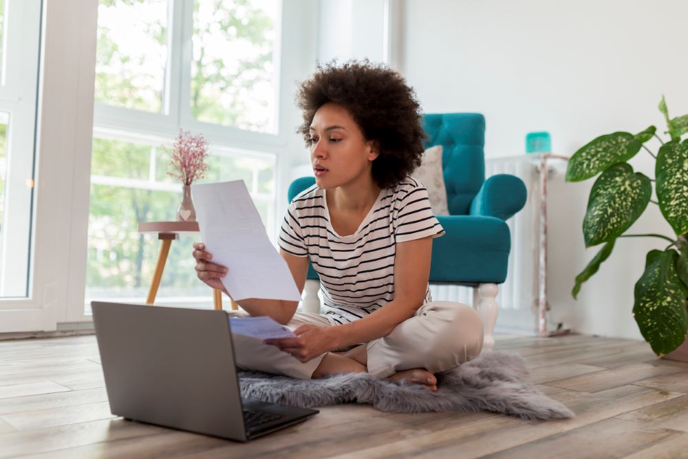 A woman on the floor with her laptop holding a paper