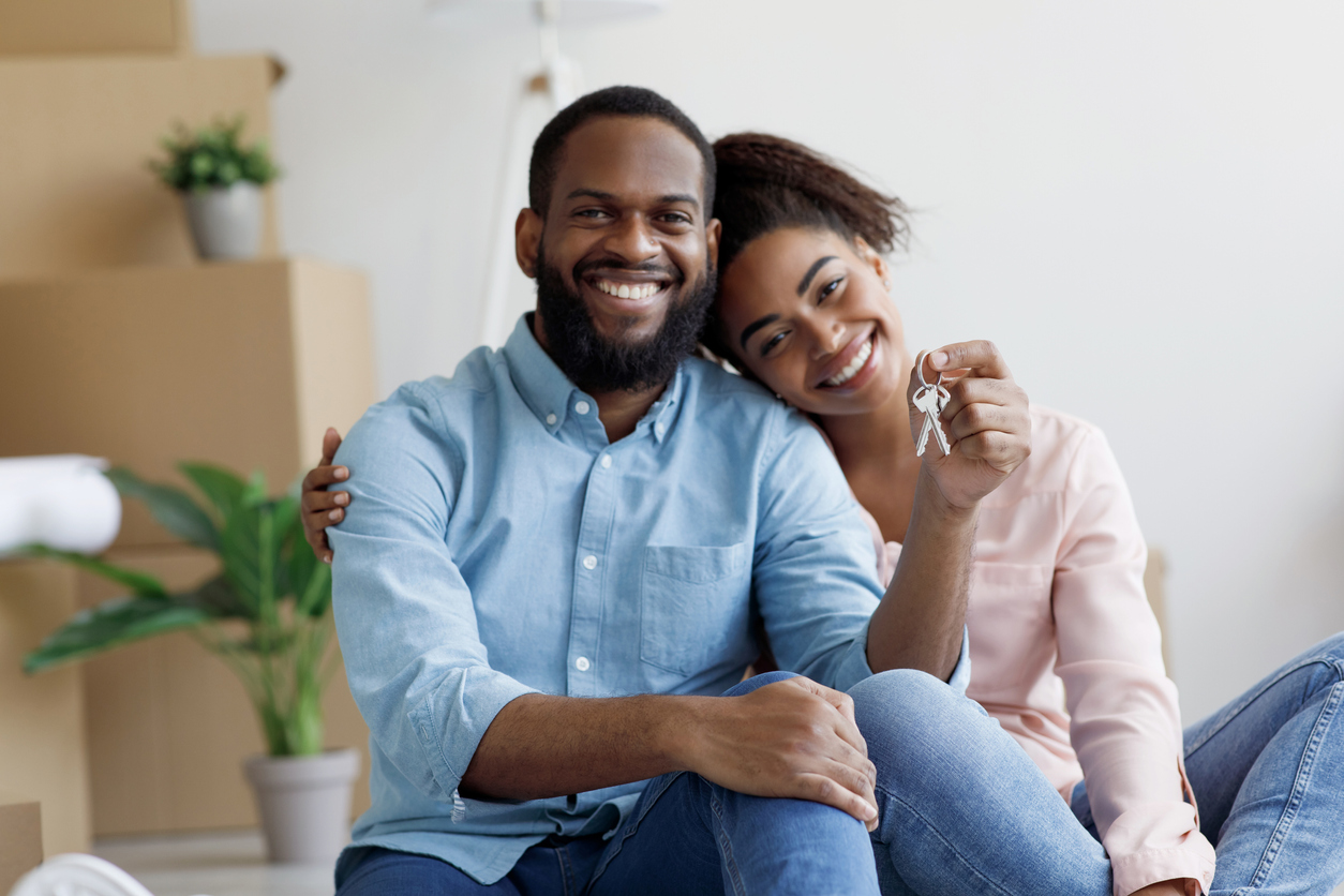 Glad cheerful young African american family show key and enjoy purchase of real estate in room with cardboard boxes holding house keys.