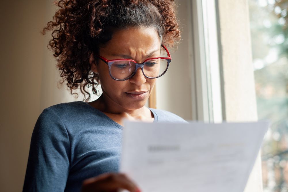 A black woman wearing glasses reading a letter.