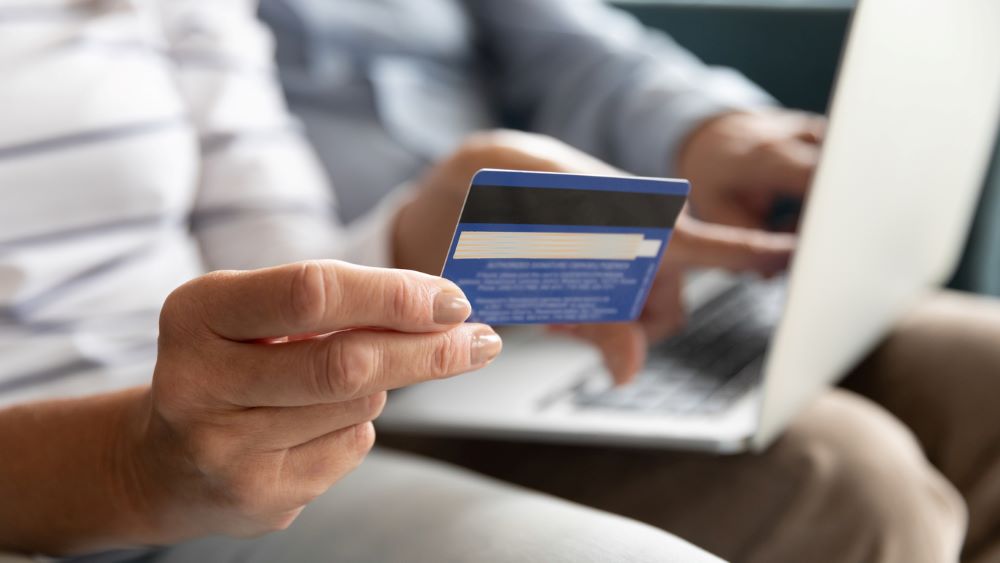 A elderly person sitting next to someone while holding a debt card.