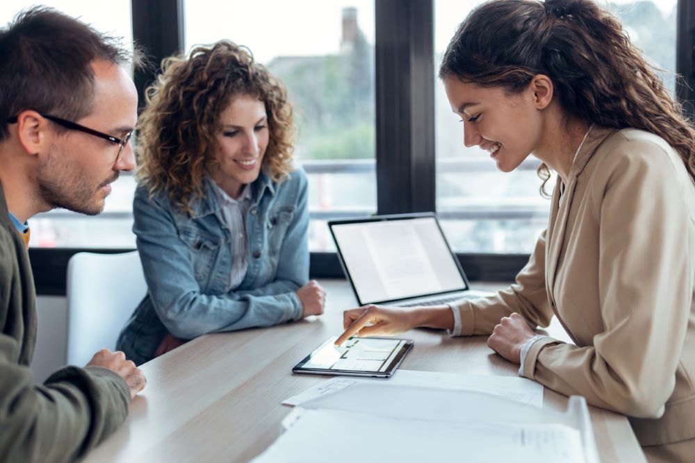 A woman lender showing a couple loan option on a tablet.