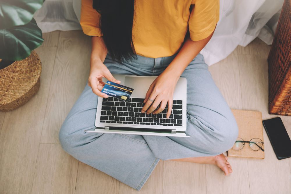 sian woman freelancer wearing yellow t-shirt using credit card and laptop.
