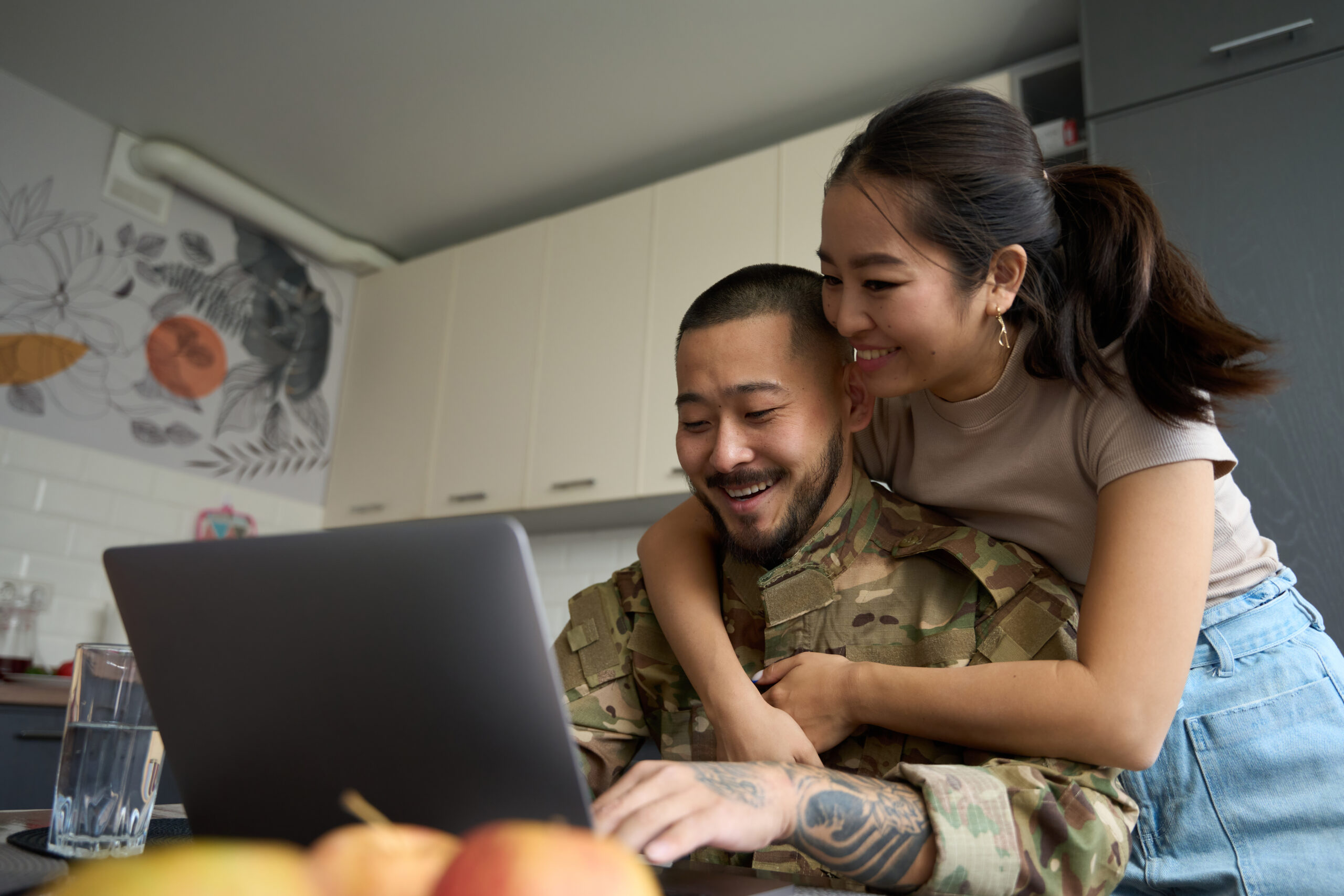 Asian woman in kitchen room hugging from back of military.