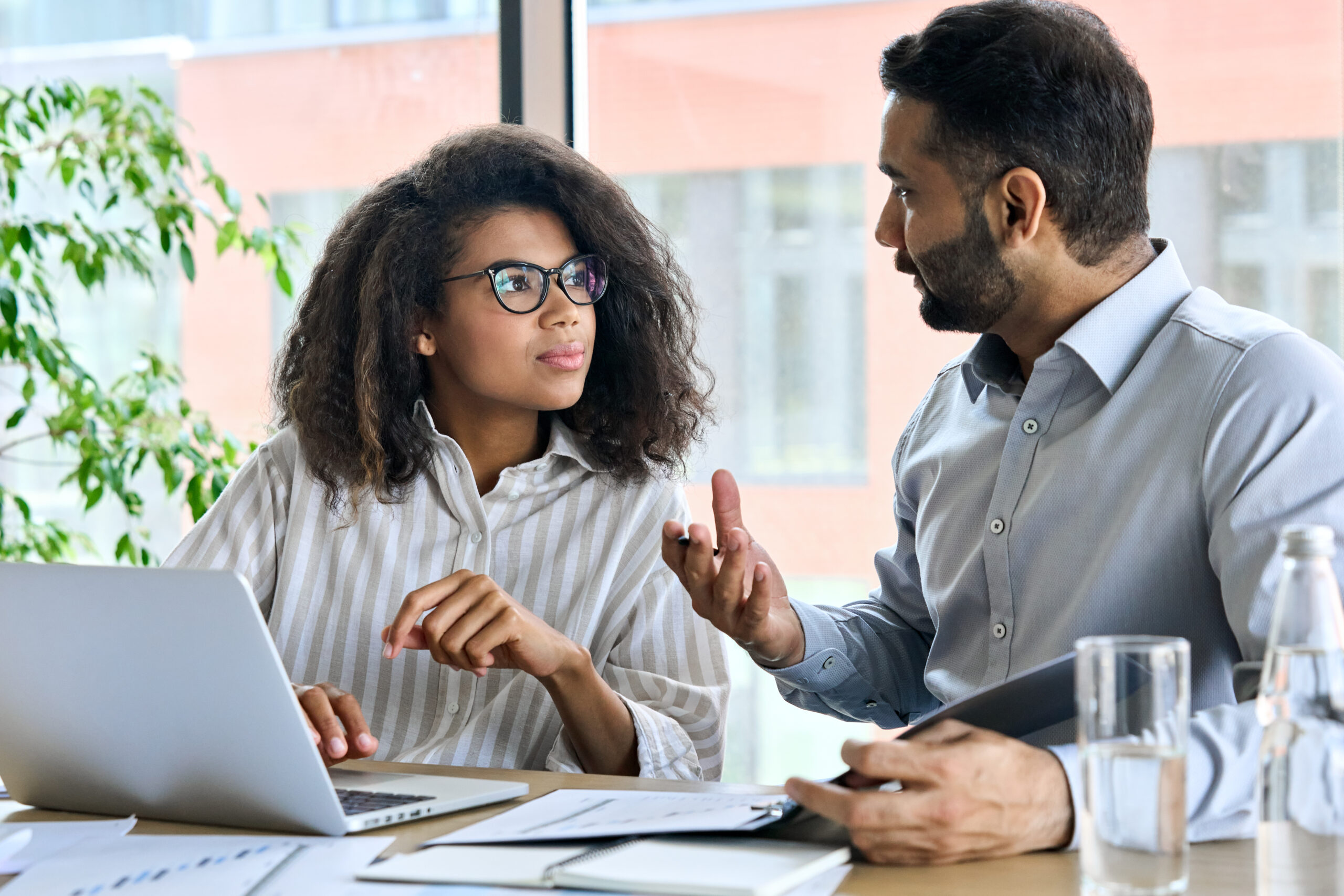 Businessman talking to female coworker, using laptop.