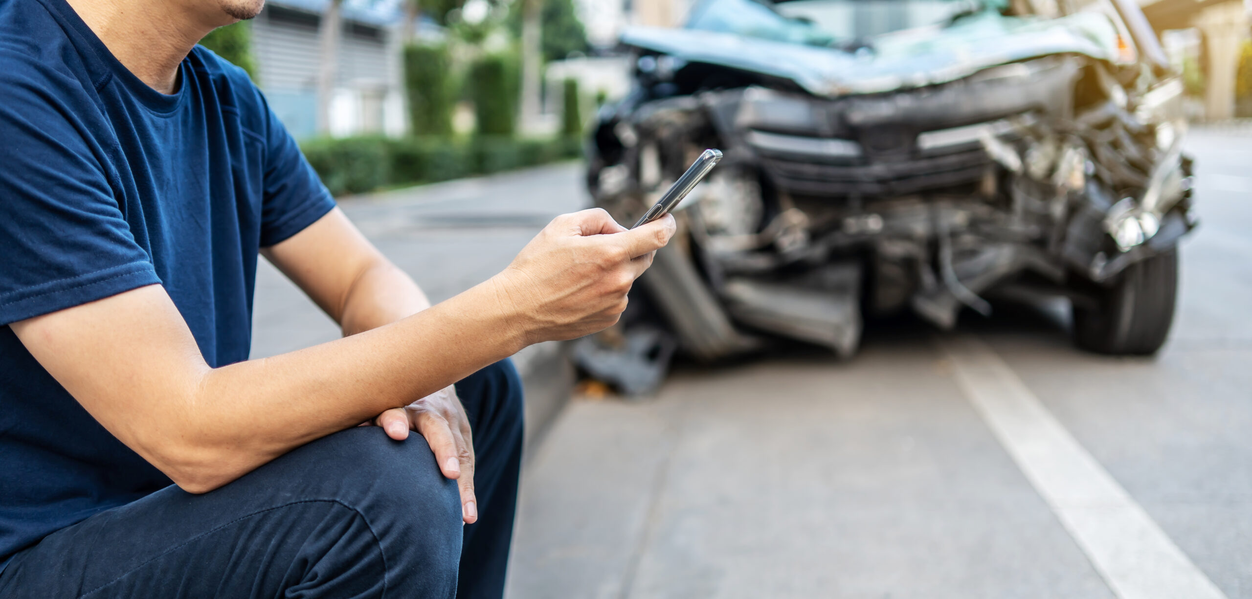 Man calling with phone to his insurance agent after traffic accident with a background of the crashed car