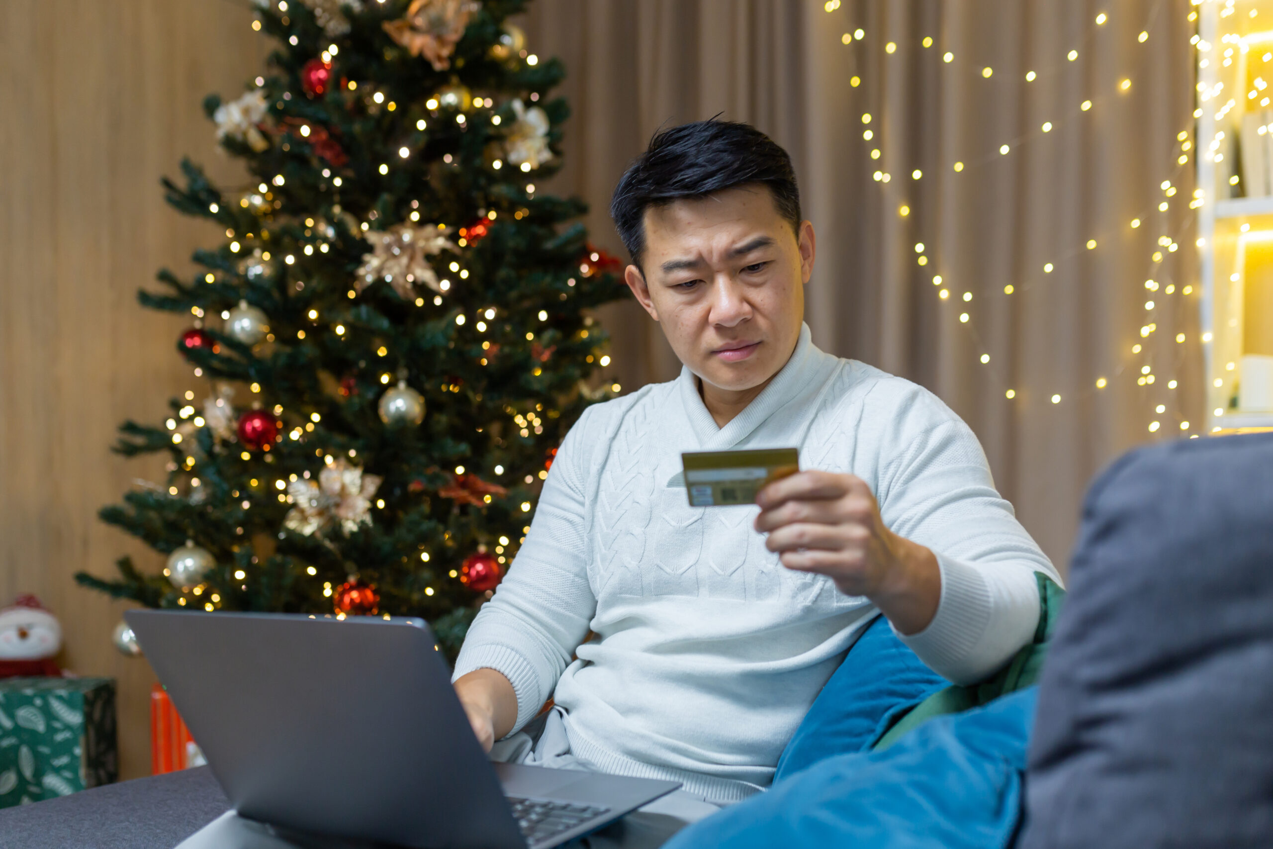 Man looking at his credit card in front of a Christmas tree